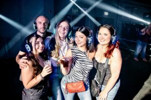 Group of friends in glowing Silent Disco Club headphones under light beams