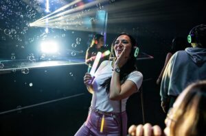 Guest dancing with a glow stick among bubbles and light beams
