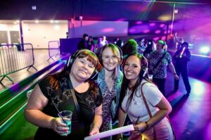 Three friends on a purple-lit silent disco dance floor