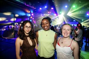 Three friends posing in silent disco headphones under stage lights