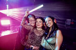 Three friends in headphones under pink light holding a light stick