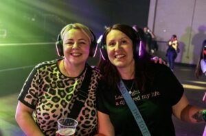 Two friends smiling in headphones under green light