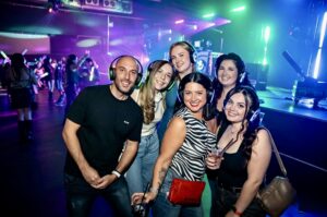 Group of six friends in silent disco headphones by the stage