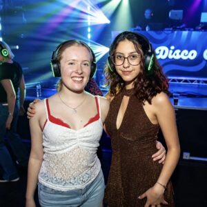 Two friends in headphones in front of the Silent Disco Club booth